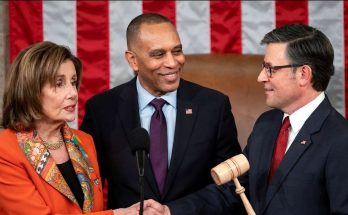 Three people in formal attire standing in front of an American flag, with one holding a