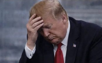 Donald Trump sitting with his head in his hand, looking down at a phone in his other