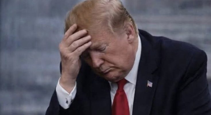 Donald Trump sitting with his head in his hand, looking down at a phone in his other