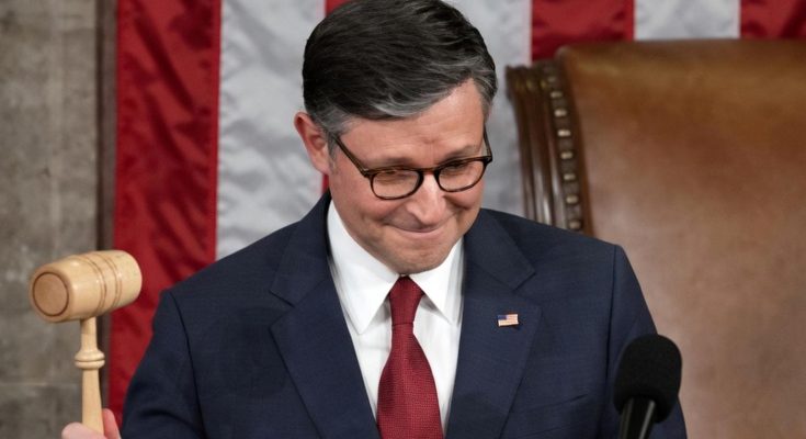 A man in a dark suit and red tie holds a wooden gavel while standing at a podium with a