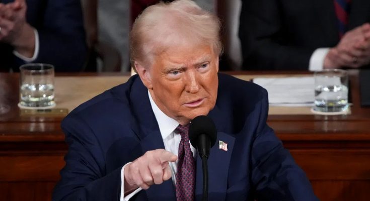 Man in suit pointing at a microphone at a wooden table