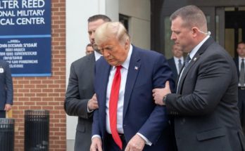 donald Trump in navy suit and red tie being escorted by Secret Service agents outside