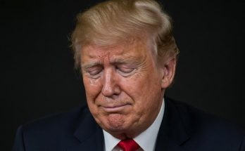donald Trump in a dark suit and red tie, eyes closed with a tear, overlaid with bold text