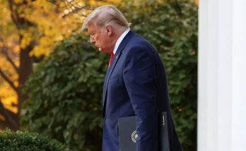 former President Donald Trump walks outside the White House holding a black folder with