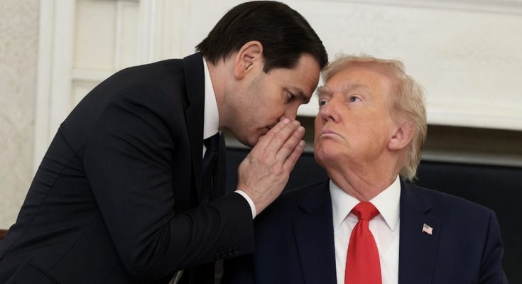 man in suit whispers secret to seated President Trump in office setting