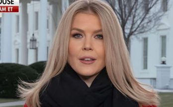 blonde woman in red coat and black scarf stands before White House columns with BREAKING