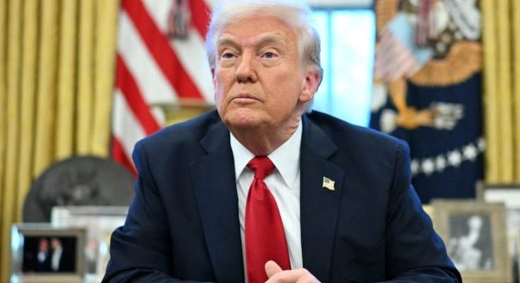 former President Donald Trump seated in the Oval Office with American flag and