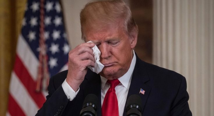 donald Trump wiping tear with tissue at podium with American flag behind him