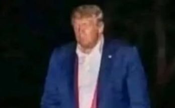donald Trump walks at night in a blue suit holding a red object