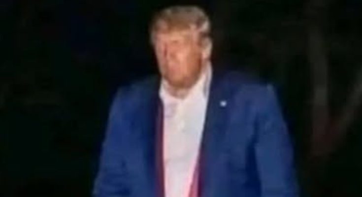 donald Trump walks at night in a blue suit holding a red object